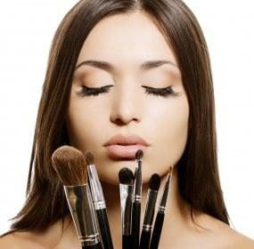 A woman with her eyes closed holding makeup brushes.
