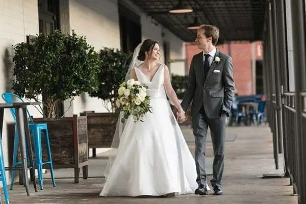 A bride and groom walking down the street holding hands.
