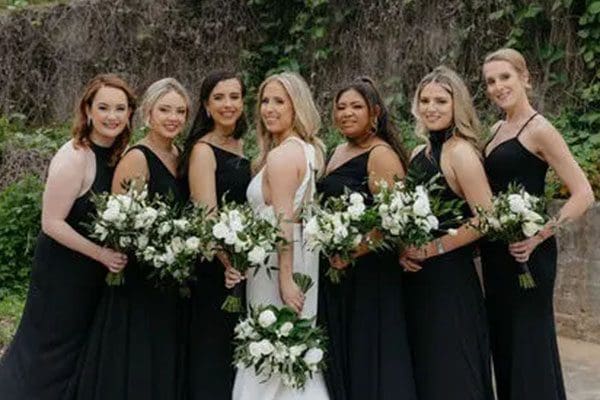 A group of women in black dresses holding white flowers.